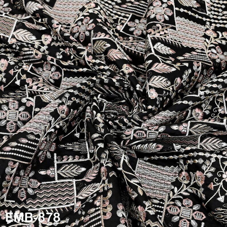May include: Black fabric with detailed embroidery in white, pink, and beige, showcasing floral and geometric motifs. The fabric is draped, creating shadows. The text "BMB 878" is visible in the lower left corner of the image.