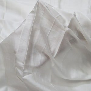 Peut inclure: Tissu blanc avec une texture lisse et soyeuse. Le tissu est plié et drapé, créant des plis et des froissures doux.