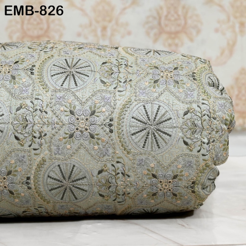 May include: A cylindrical decorative pillow with an intricate embroidered pattern. The fabric is a pale green with detailed floral and geometric designs in shades of gray, green, and gold. The text "EMB-826" is visible in the upper left corner.