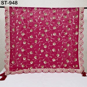 Puede incluir: Una bufanda transparente de color magenta con intrincados bordados florales dorados y un borde festoneado. La bufanda tiene borlas decorativas en las esquinas y el texto "ST-948" en la esquina superior izquierda.