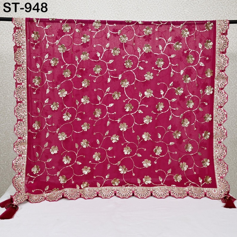 Puede incluir: Una bufanda transparente de color magenta con intrincados bordados florales dorados y un borde festoneado. La bufanda tiene borlas decorativas en las esquinas y el texto "ST-948" en la esquina superior izquierda.