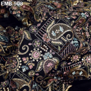 Puede incluir: Tela negra con intrincados bordados en dorado, rosa, azul y verde. El diseño incluye patrones de cachemira y florales, con el texto "EMB-908". La tela tiene una apariencia lujosa y texturizada, ideal para proyectos textiles.