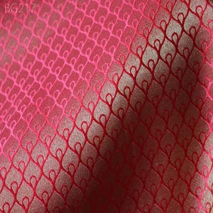 May include: Close-up of a red fabric with a woven pattern of small, interlocking loops. The fabric has a subtle sheen and a slightly textured surface.