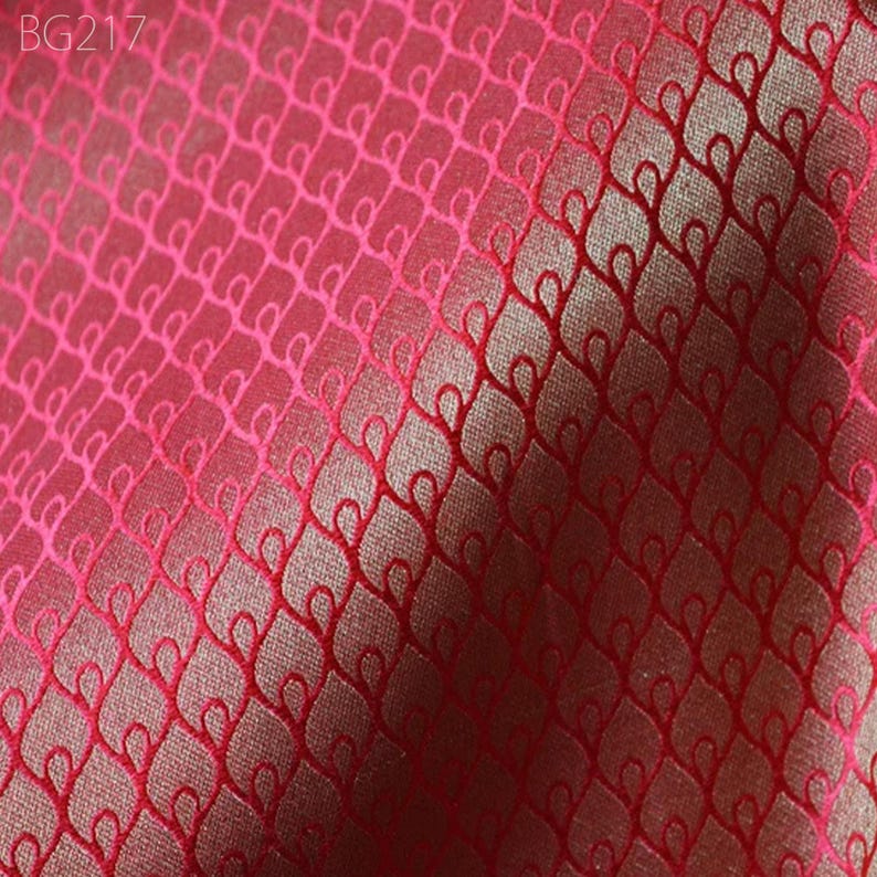 May include: Close-up of a red fabric with a woven pattern of small, interlocking loops. The fabric has a subtle sheen and a slightly textured surface.