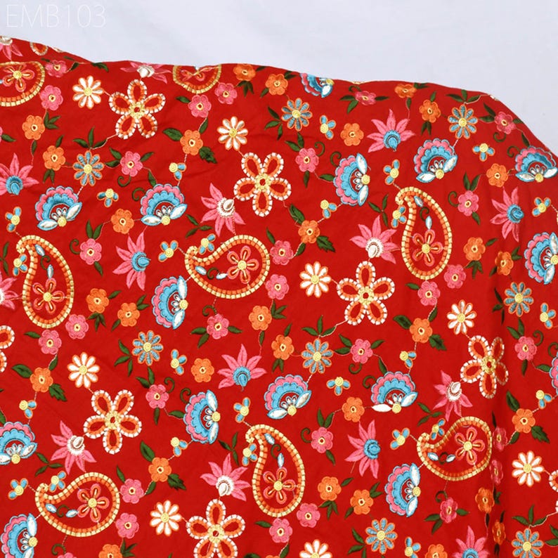 May include: Red fabric with a paisley and floral pattern. The fabric is embroidered with colorful flowers and paisley shapes.