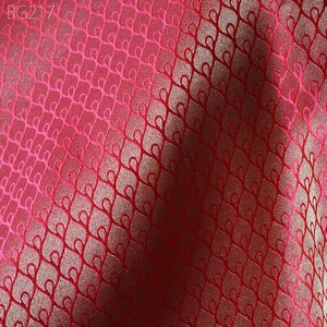 May include: Red fabric with a repeating pattern of small, stylised hearts. The fabric has a subtle sheen and a slightly textured surface.