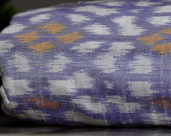 May include: A close-up of a folded fabric with a white and purple ikat pattern. The fabric has a subtle sheen and a textured surface.