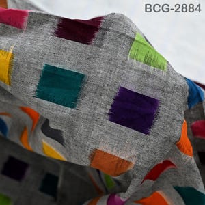 Puede incluir: Una tela gris con un patrón repetitivo de formas rectangulares coloridas en tonos de morado, verde, naranja, amarillo y rosa. La tela tiene un aspecto texturizado y está ligeramente doblada, revelando el diseño. El texto "BCG-2884" es visible.