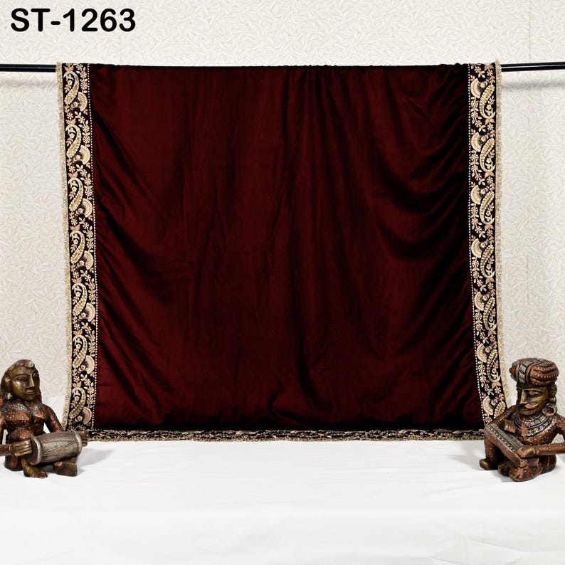 May include: A burgundy velvet textile with ornate gold and black embroidered borders. The textile is draped over a rod, with the text "ST-1263" in the upper left corner. Decorative statues flank the textile.
