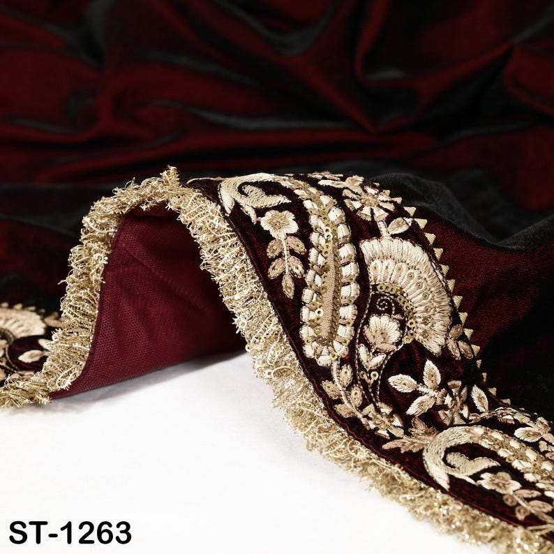 May include: Close-up of a burgundy fabric with intricate gold embroidery and a gold fringe trim. The fabric has a velvet-like texture and features floral and leaf patterns. The text "ST-1263" is visible at the bottom.