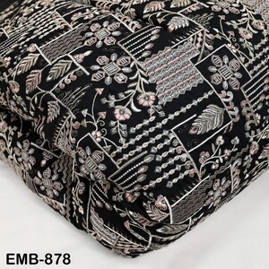 May include: Black fabric with detailed embroidery, displaying floral and geometric designs in pink, silver, and white. The fabric is folded, revealing the intricate pattern. The text "EMB-878" is visible in the bottom left corner.