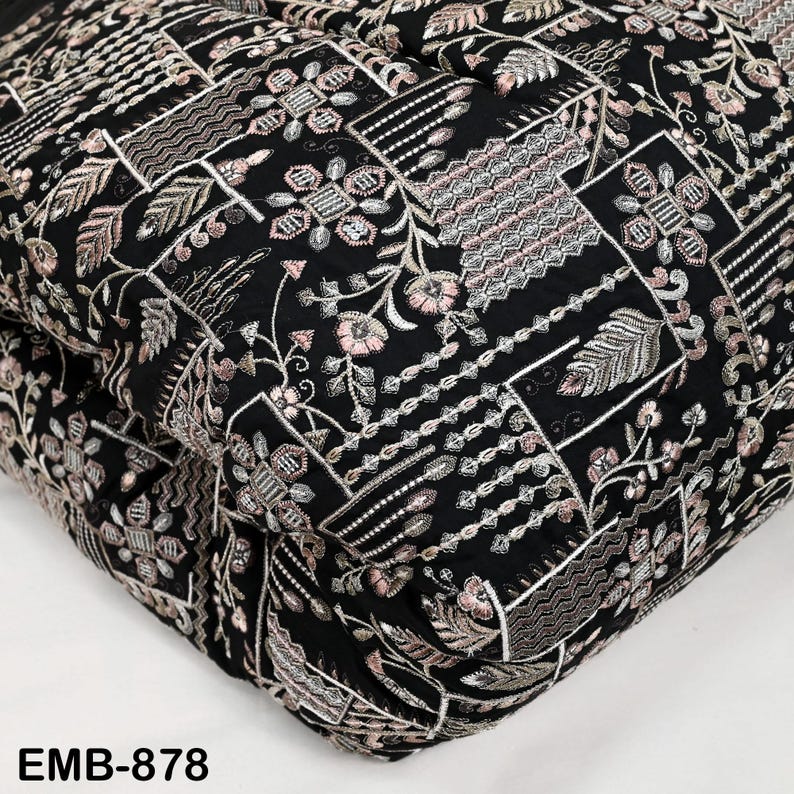 May include: Black fabric with detailed embroidery, displaying floral and geometric designs in pink, silver, and white. The fabric is folded, revealing the intricate pattern. The text "EMB-878" is visible in the bottom left corner.