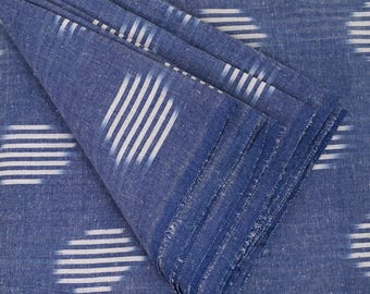 May include: Close-up of a folded blue fabric with a white ikat pattern. The fabric has a textured surface and a subtle sheen. The fabric is folded in a way that shows the layers of the fabric. The fabric is labelled with the code BCG-2818.