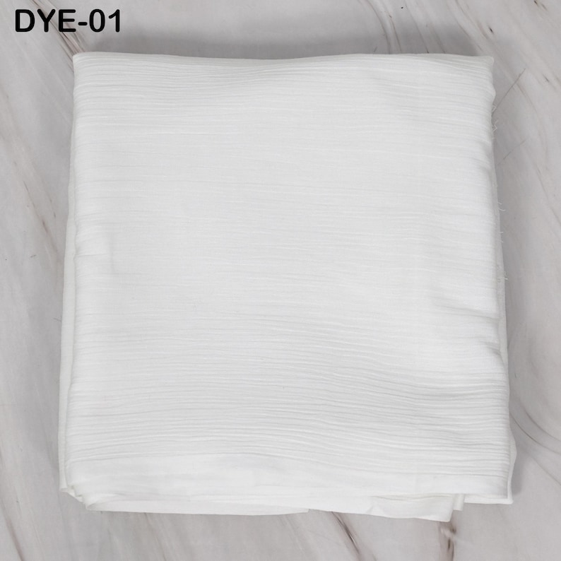 May include: A folded, white fabric with a textured, ribbed surface. The fabric is rectangular and appears to be a textile, possibly for clothing or home decor. The text "DYE-01" is in the upper left corner.