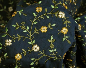 May include: Dark blue fabric with embroidered floral vines in shades of green and yellow. The fabric has a subtle texture and a slightly wrinkled appearance.