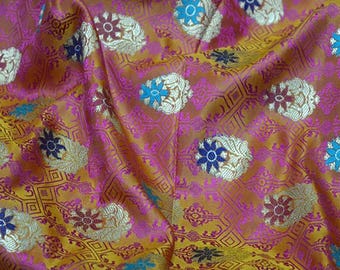 Puede incluir: Primer plano de una tela vibrante con un patrón floral repetido. La tela presenta una mezcla de colores, incluyendo dorado, rosa y azul. El diseño floral se establece sobre un fondo geométrico, creando una apariencia texturizada. El texto "BG1835" es visible en la esquina superior izquierda.