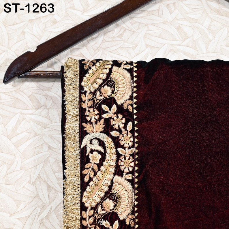 May include: A section of a maroon textile with intricate gold embroidery and a gold fringe trim. The design includes floral and paisley patterns. The textile is hanging on a wooden hanger. The text "ST-1263" is visible.