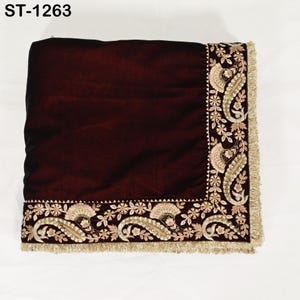 May include: A burgundy velvet textile with intricate gold and beige embroidery along the edges. The design includes paisley and floral patterns, with a fringe trim. The text "ST-1263" is in the upper left corner.