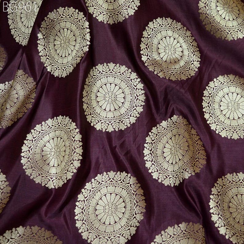 May include: Purple fabric with a repeating pattern of gold circular designs. The designs feature intricate details and a floral motif.