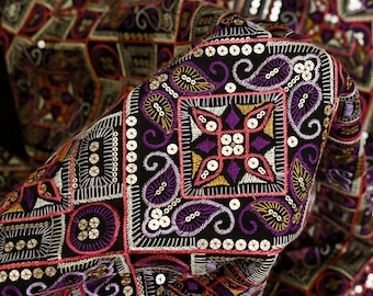 May include: Black fabric with intricate embroidery in shades of purple, pink, gold, and white. The fabric is adorned with sequins and features a geometric pattern.