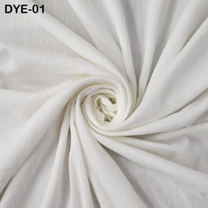 May include: A close-up of a white fabric with a textured, rippled surface. The fabric is arranged in a swirling pattern, with the center forming a tight spiral. The text "DYE-01" is in the upper left corner.