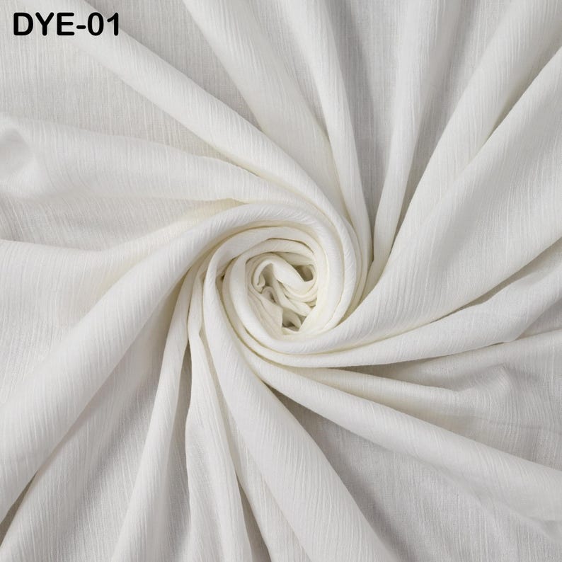 May include: A close-up of a white fabric with a textured, rippled surface. The fabric is arranged in a swirling pattern, with the center forming a tight spiral. The text "DYE-01" is in the upper left corner.
