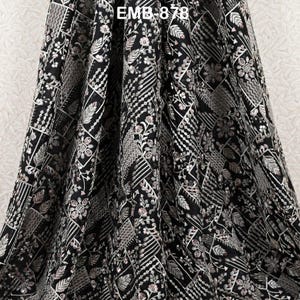 May include: Black fabric with detailed embroidery. The design includes geometric shapes, floral patterns, and leaf motifs in silver and white thread. The text "EMB 878" is visible at the top of the fabric.