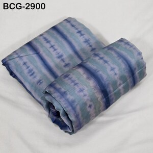 Può includere: Un tessuto piegato con un motivo tie-dye blu e verde acqua. Il tessuto è disposto in diagonale, con la parte superiore ripiegata su quella inferiore. Il testo "BCG-2900" è nell'angolo in alto a sinistra.