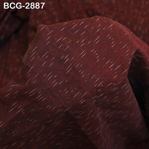 May include: Close-up of a burgundy fabric with a subtle texture and white diagonal lines. The fabric has a slightly wrinkled appearance, with the text "BCG-2887" in the upper left corner. The material appears to be soft and pliable.