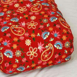 May include: Red fabric with embroidered paisley and floral patterns in shades of orange, pink, blue, and yellow.