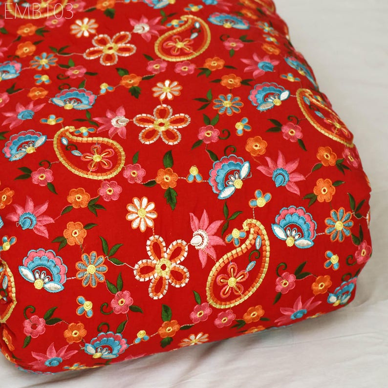 May include: Red fabric with embroidered paisley and floral patterns in shades of orange, pink, blue, and yellow.