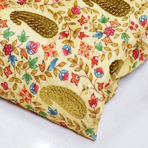 Könnte beinhalten: Ein gelber Stoff mit einem Blumenmuster und goldenen Pailletten. Der Stoff ist in der Mitte gefaltet und das Muster ist auf beiden Seiten sichtbar.