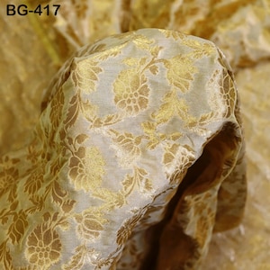 Puede incluir: Primer plano de una tela blanca con un patrón floral dorado. La tela es texturizada y tiene un brillo sutil. La tela está etiquetada como "BG-417".