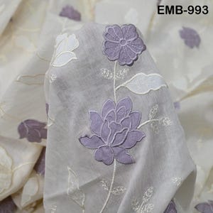 Op de afbeelding: Transparante stof met geborduurd bloemmotief. De stof heeft grote, lavendelkleurige bloemen met gedetailleerde steken, samen met witte en lavendelkleurige accenten. De tekst "EMB-993" is zichtbaar in de rechterbovenhoek.
