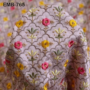 以下が含まれることがあります： ピンクの生地のクローズアップ。黄色とピンクの刺繍の花が繰り返しパターンで施されています。生地は控えめな光沢と柔らかな質感があります。画像の左上隅に「EMB-765」というテキストが表示されています。