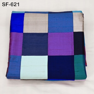 Può includere: Un tessuto quadrato piegato con un design patchwork. Il tessuto presenta una griglia di quadrati nelle tonalità di blu, viola, verde acqua e argento. Il testo "SF-621" si trova nell'angolo in alto a sinistra.