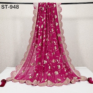 Puede incluir: Una bufanda magenta con bordado floral dorado y un borde dorado festoneado. La bufanda tiene una apariencia delicada y transparente y est&aacute; adornada con peque&ntilde;as borlas en los extremos. El texto "ST-948" est&aacute; en la esquina superior izquierda.