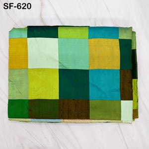 May include: A folded patchwork textile with a variety of green, teal, and gold squares. The textile is labeled "SF-620" in the upper left corner. The squares are arranged in a grid pattern, creating a geometric design.