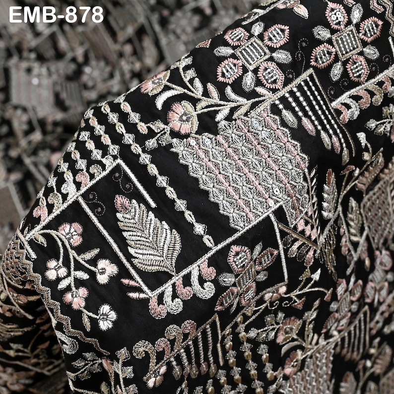 May include: Close-up of black fabric with detailed embroidery. The design incorporates floral and geometric patterns in pink, silver, and white. The fabric has a luxurious appearance, with detailed stitching and a textured surface. The text "EMB-878" is visible in the top left corner.