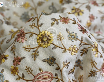 Puede incluir: Tela blanca con un patrón de bordado floral en tonos de rosa, azul, amarillo y marrón. La tela tiene un brillo sutil y una textura delicada.