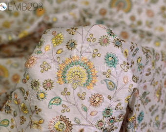 Puede incluir: Primer plano de una tela blanca con un patrón floral bordado en hilo dorado, verde y rosa. La tela tiene un brillo sutil y una textura delicada.