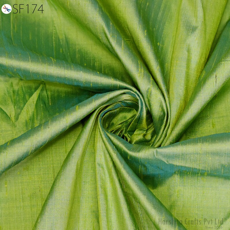 May include: A close-up of a green and blue silk fabric with a subtle sheen. The fabric is folded and draped, showcasing its texture and drape.