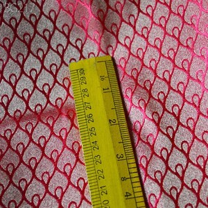 May include: Close-up of a pink fabric with a repeating pattern of red hearts. A yellow ruler is placed on the fabric, showing measurements in inches.