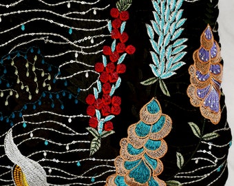 May include: Black fabric with colorful embroidered floral designs. The fabric features a variety of flowers, leaves, and other patterns in shades of red, blue, green, and yellow.