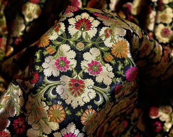 May include: Black fabric with a gold and colorful floral pattern. The fabric has a brocade texture and is woven with intricate details.