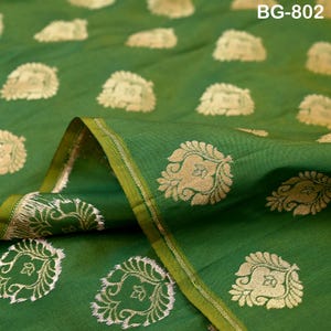 Peut inclure: Un tissu vert vif présentant un motif répétitif de fleurs dorées métalliques. Le textile présente un bord plié avec une bordure finie. Le texte BG-802 est visible dans le coin supérieur droit de l'image, indiquant le code du produit.