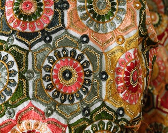 May include: White fabric with a repeating pattern of embroidered floral motifs in shades of pink, green, gold, and black.