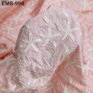 Op de afbeelding: Roze stof met witte geborduurde bloempatronen. De stof is opgevouwen, waardoor de textuur en het ontwerp zichtbaar zijn. De tekst "EMB-998" is zichtbaar. De borduursels tonen gedetailleerde, stervormige bloemmotieven.