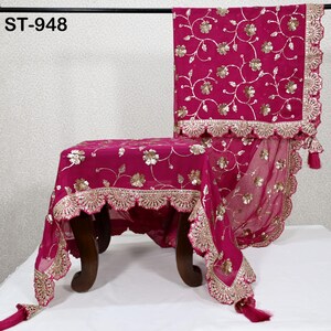 Puede incluir: Textil magenta drapeado sobre una silla, con bordado floral dorado y borde festoneado dorado. La tela tiene borlas y el texto "ST-948" es visible.