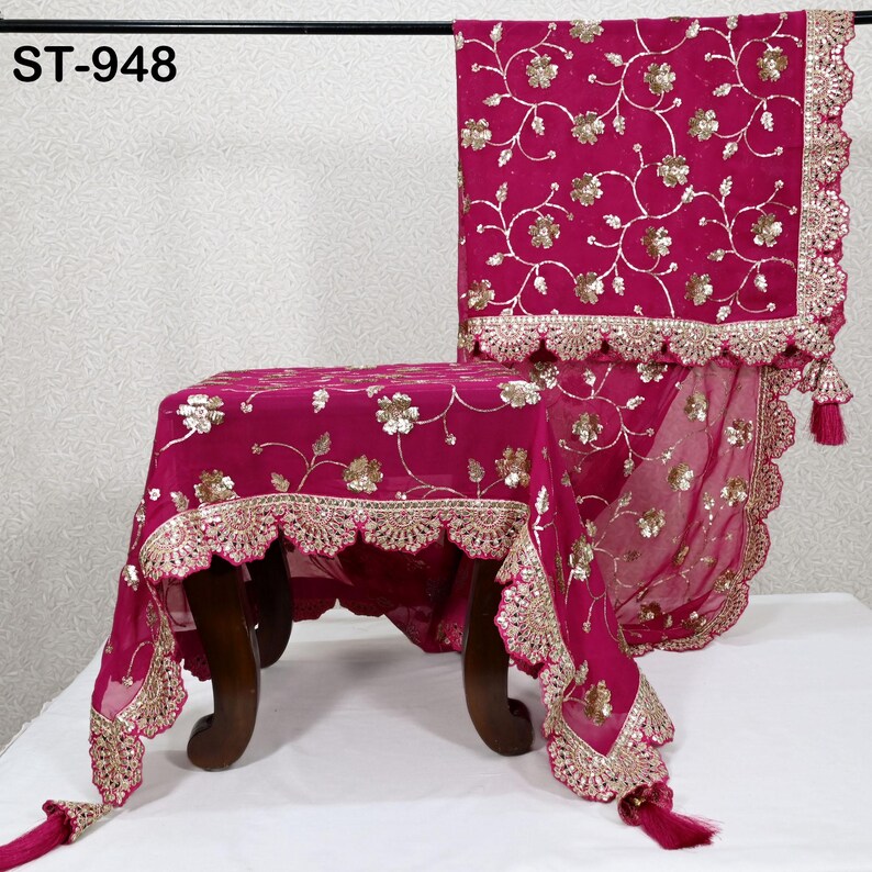 Puede incluir: Textil magenta drapeado sobre una silla, con bordado floral dorado y borde festoneado dorado. La tela tiene borlas y el texto "ST-948" es visible.
